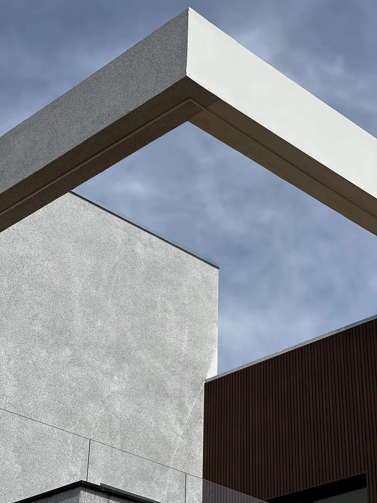 Detalhe da fachada: pórtico branco, concreto em textura e painel ripado de madeira recortados contra o céu